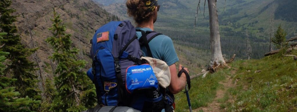Man with a hiking backpack walking in the mountains during a summer trek, carrying travel equipment in a natural landscape.