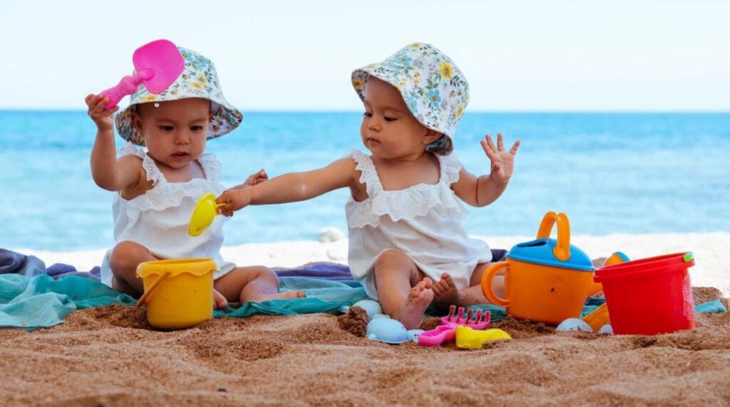 Bimbe che giocano sulla sabbia durante una vacanza al mare, protette dal sole e impegnate in attività all’aperto.