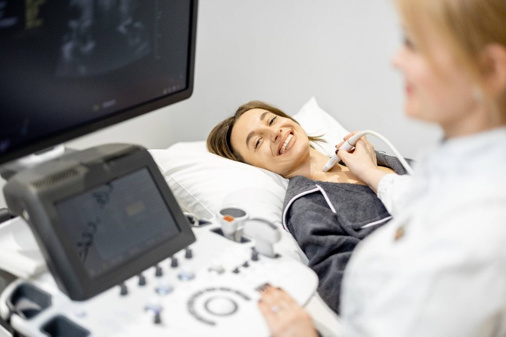 Medico specialista che esegue un'ecografia al collo del paziente posizionando la sonda per analizzare la struttura della tiroide.